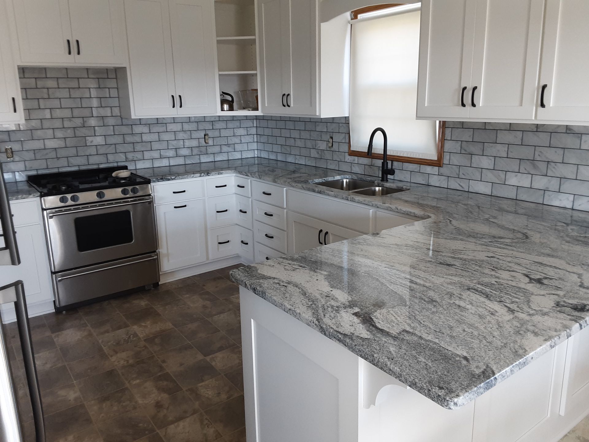 White kitchen with stainless steel appliances, granite countertops, and blue tile backsplash.