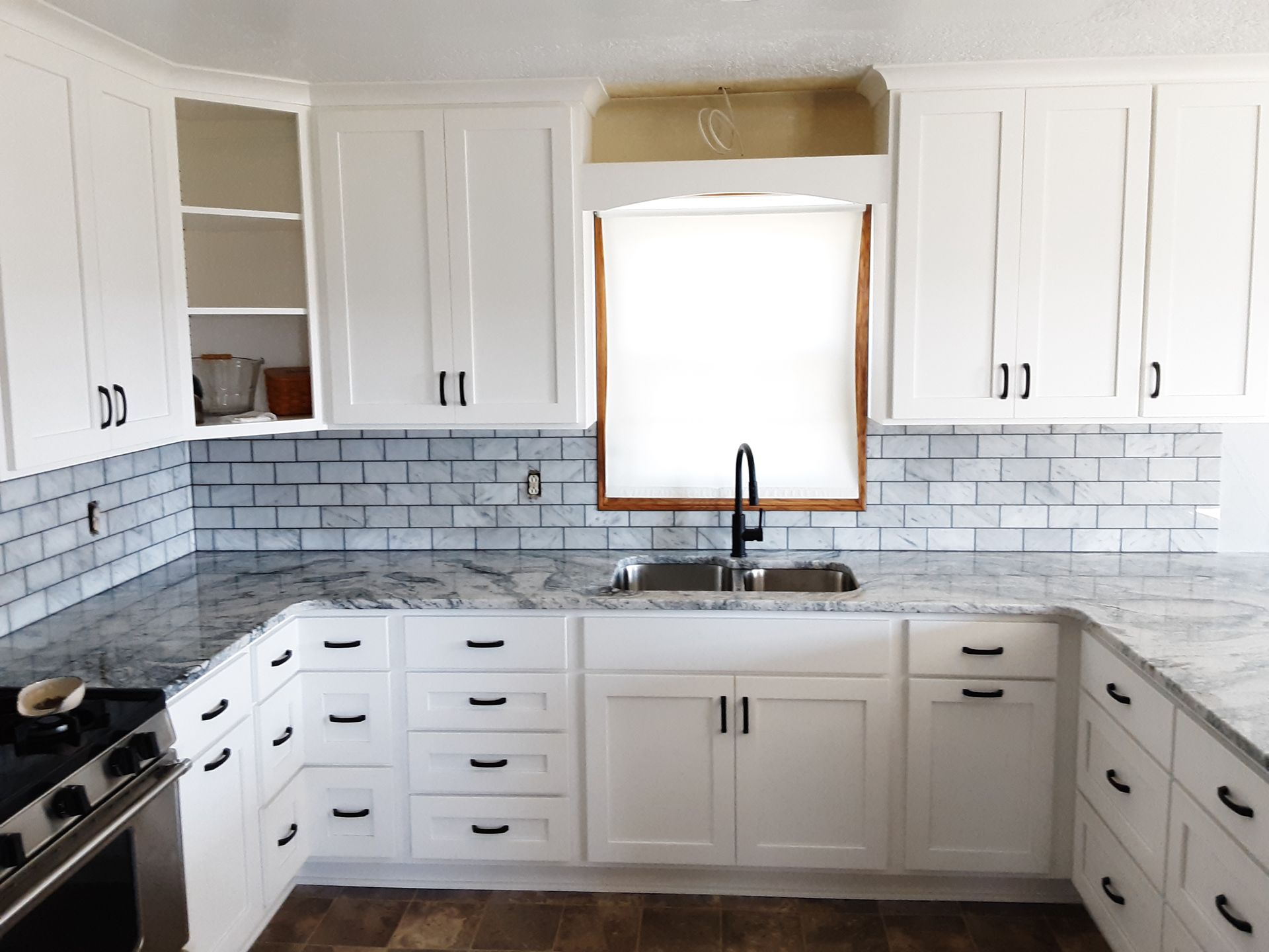 White kitchen cabinets, granite countertops, subway tile backsplash, and a black faucet.