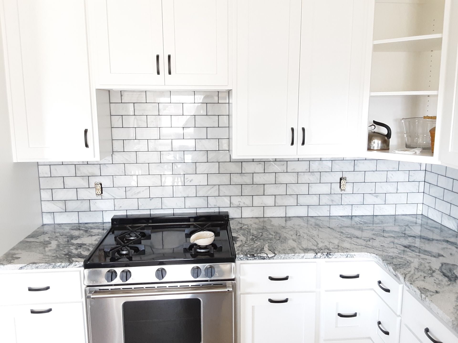 White kitchen with granite countertops, stainless steel stove, and white cabinets with black hardware.