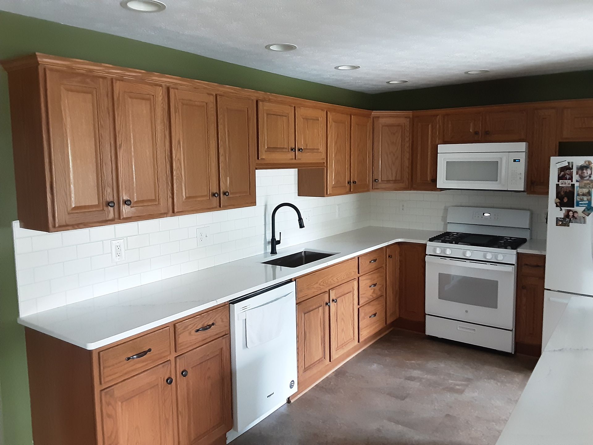 Kitchen with light-colored wood cabinets, white countertops, and white appliances. Black faucet.