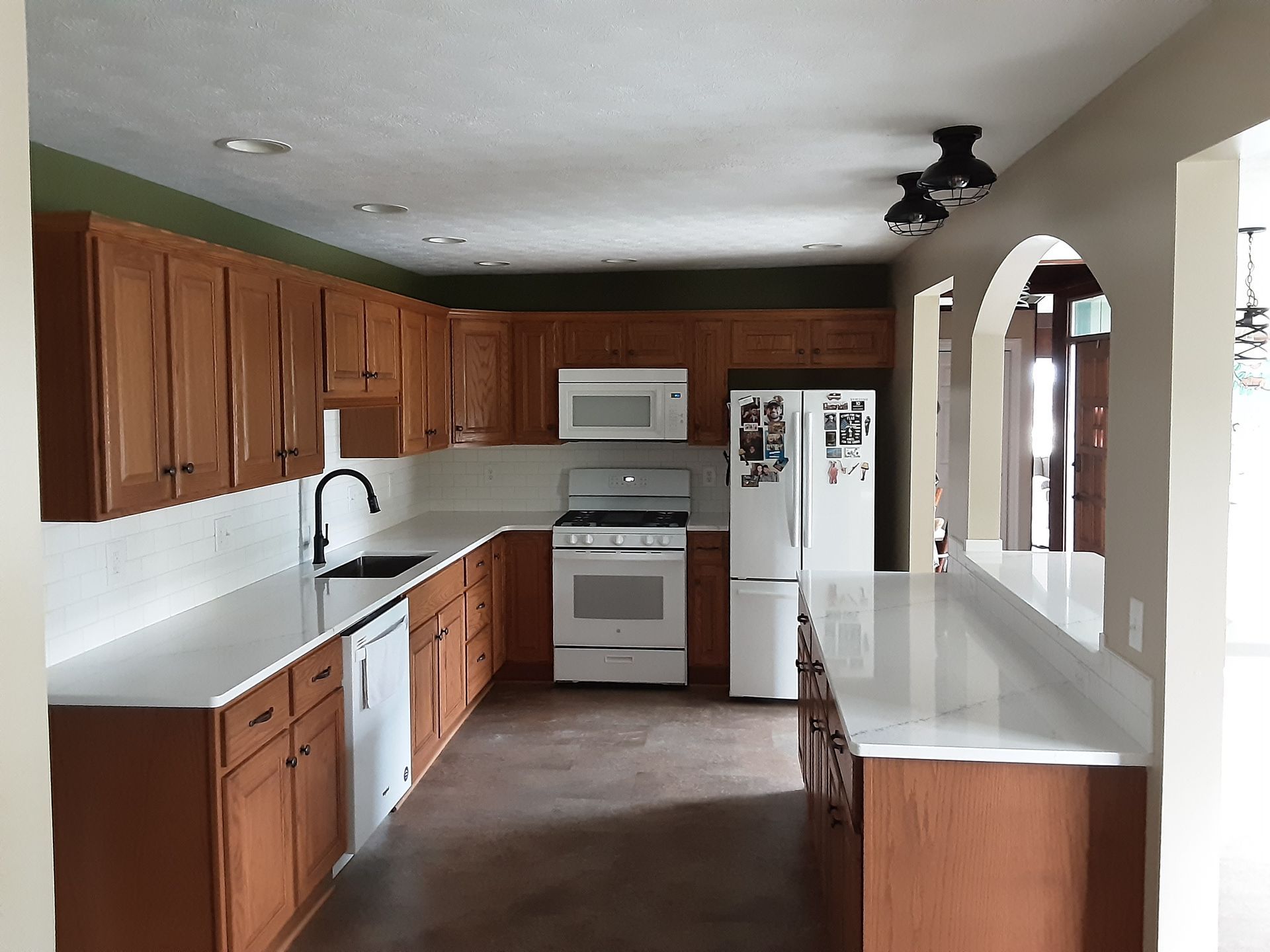 U-shaped kitchen with light countertops, wood cabinets, white appliances, and a central island.