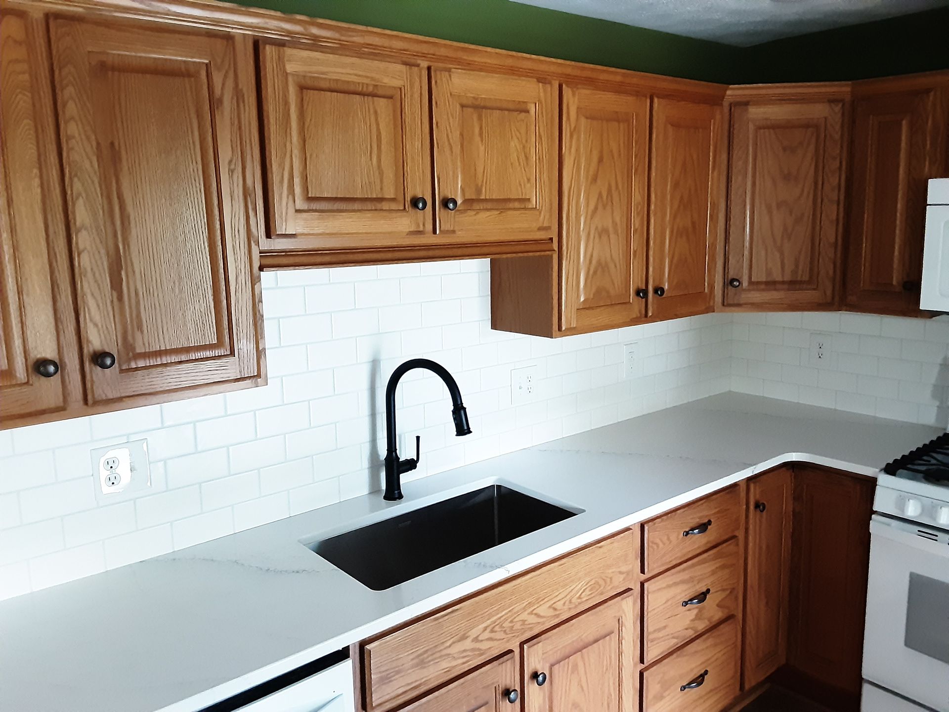 Kitchen with light cabinets, white countertop, black faucet, and white subway tile backsplash.
