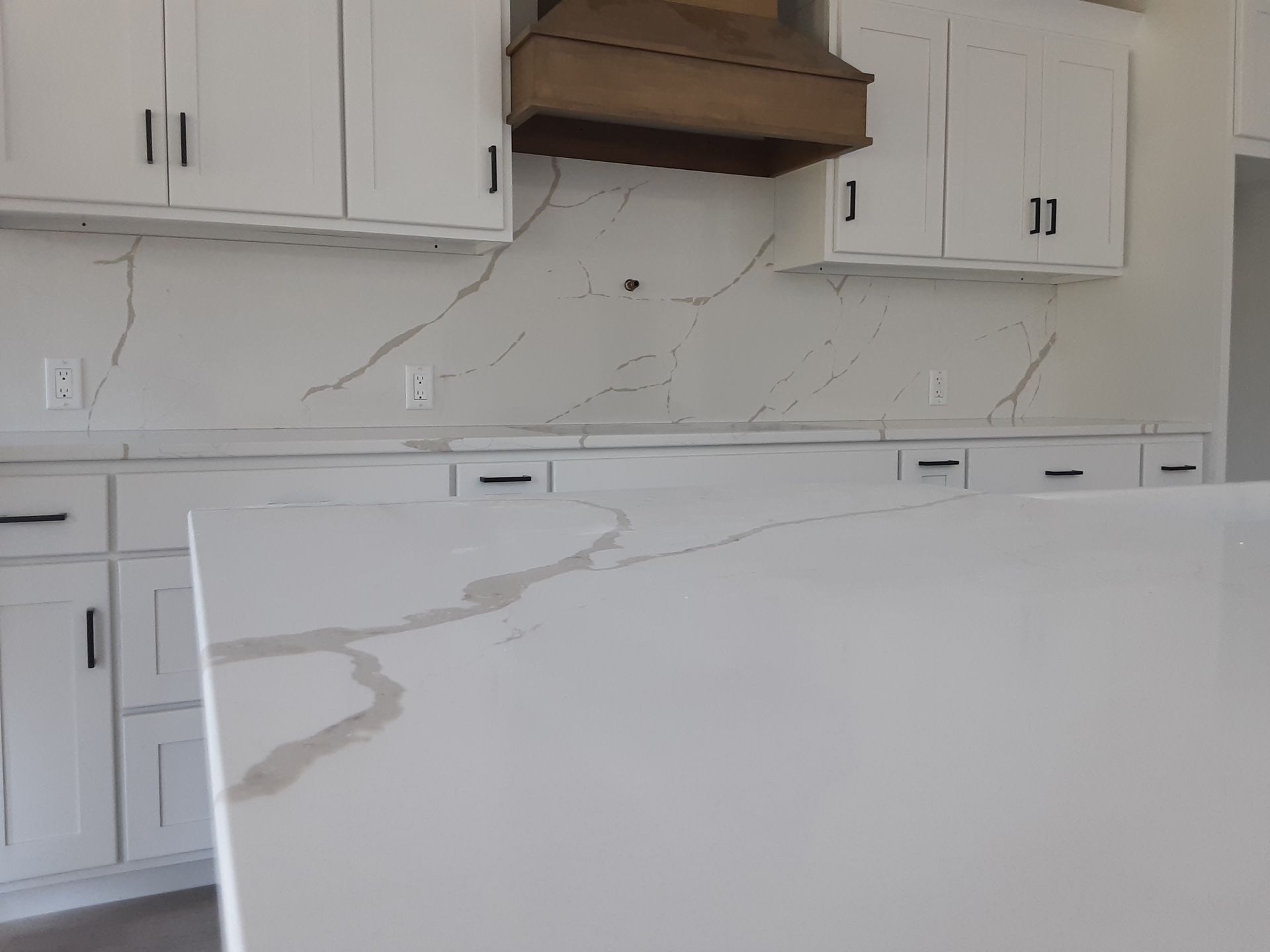 White kitchen with marble-look countertops, cabinets, and a range hood.