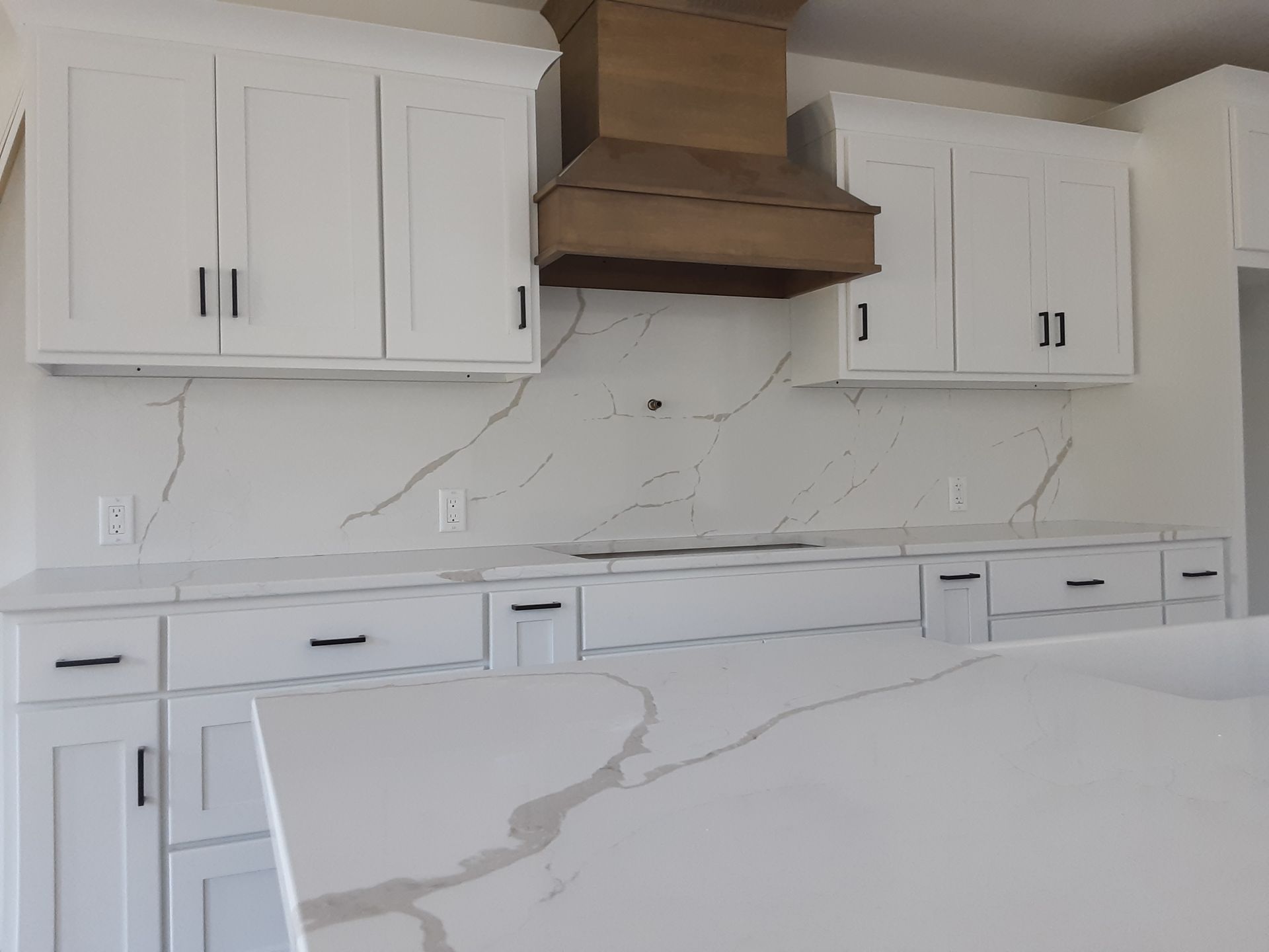 White kitchen with cabinets, countertops, and range hood.
