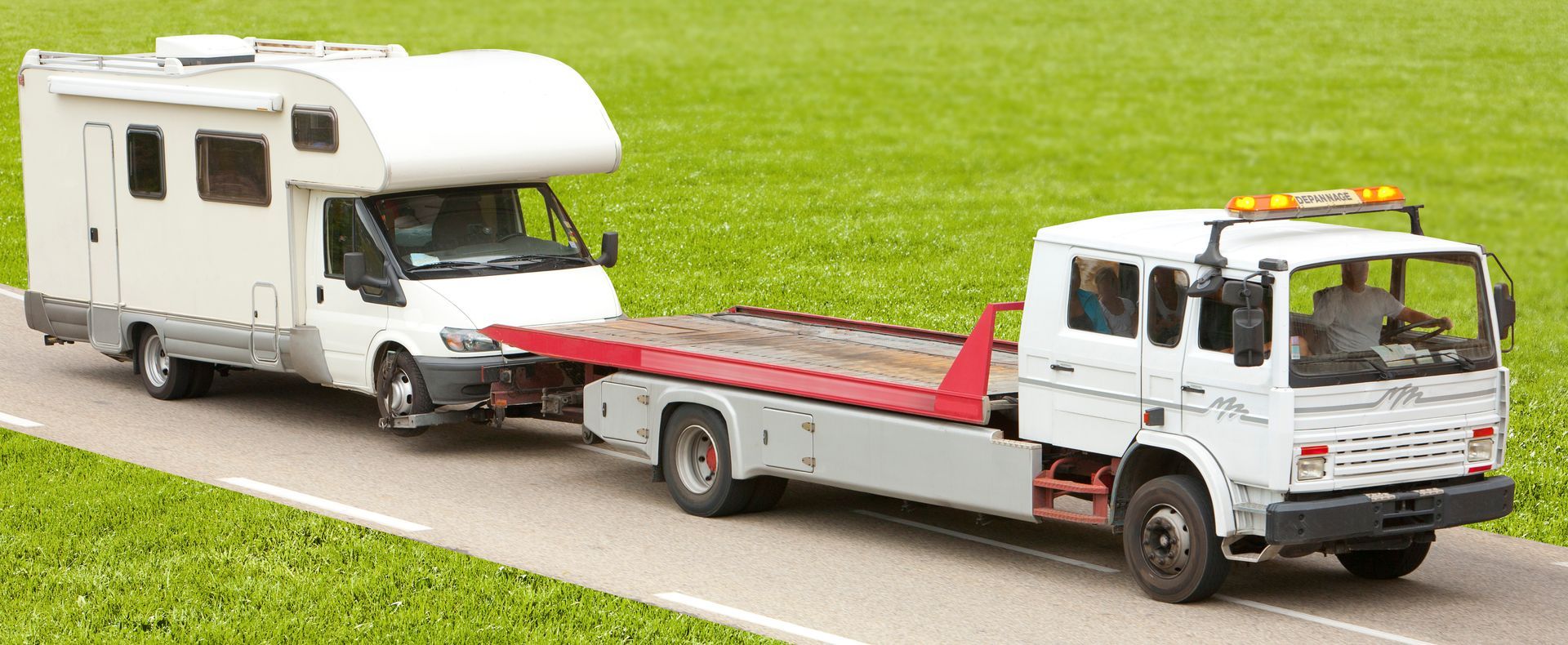 A tow truck is towing a camper down a road.