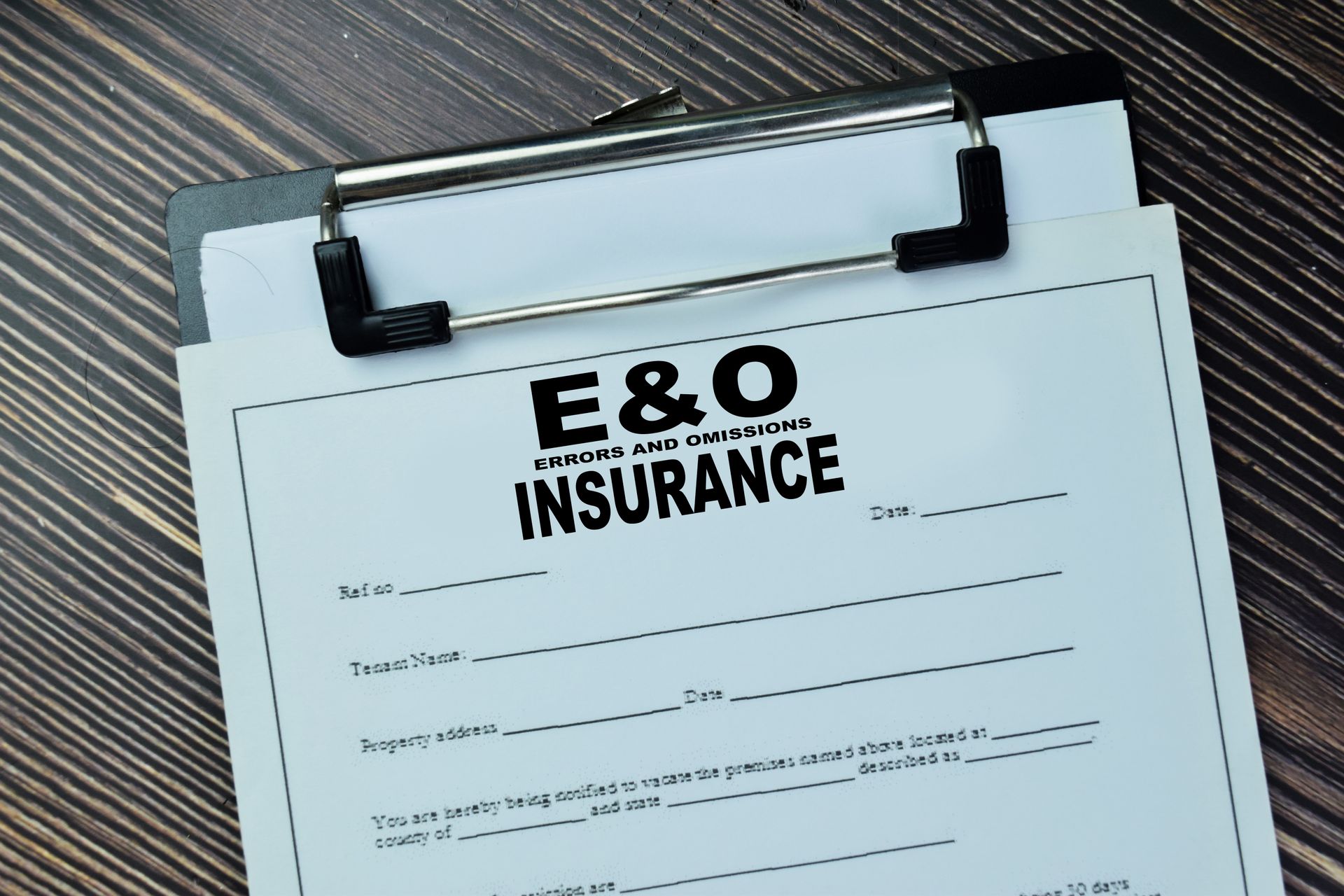 An e & o insurance form is on a clipboard on a wooden table.