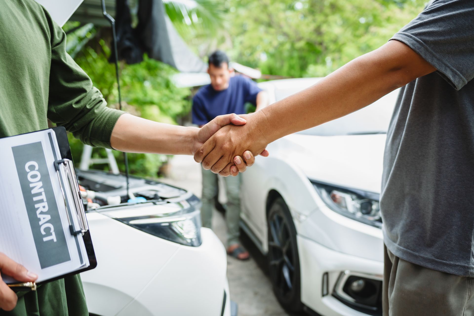 A man is shaking hands with a car dealer in front of a white car.