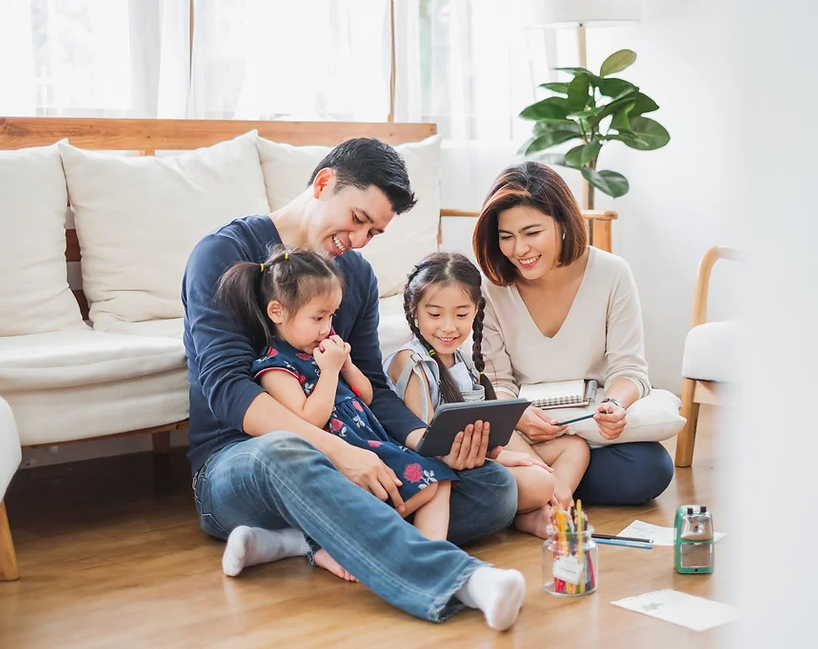 A family is sitting on the floor in a living room looking at a tablet.