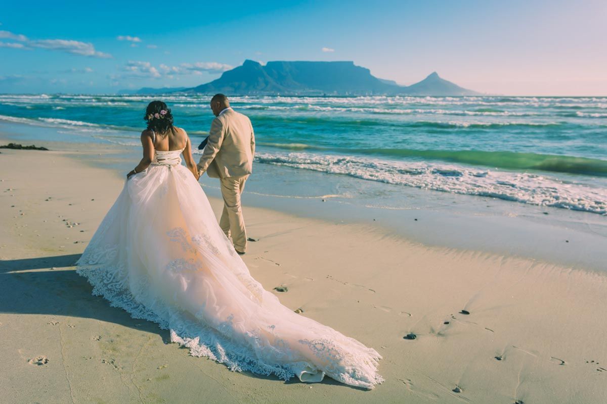 A bride and groom are walking on the beach holding hands.