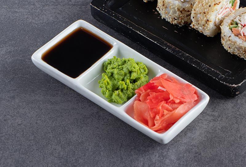 A tray of sushi sauce , wasabi , and ginger on a table.