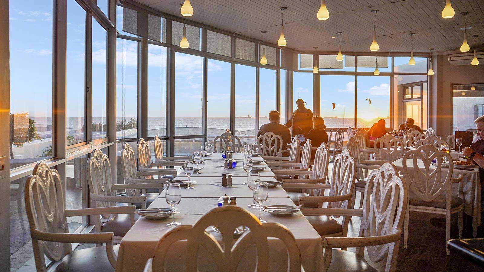 A restaurant with tables and chairs and a view of the ocean.