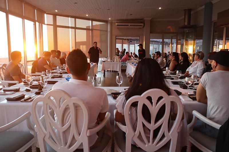 A group of people are sitting at tables in a restaurant at sunset.