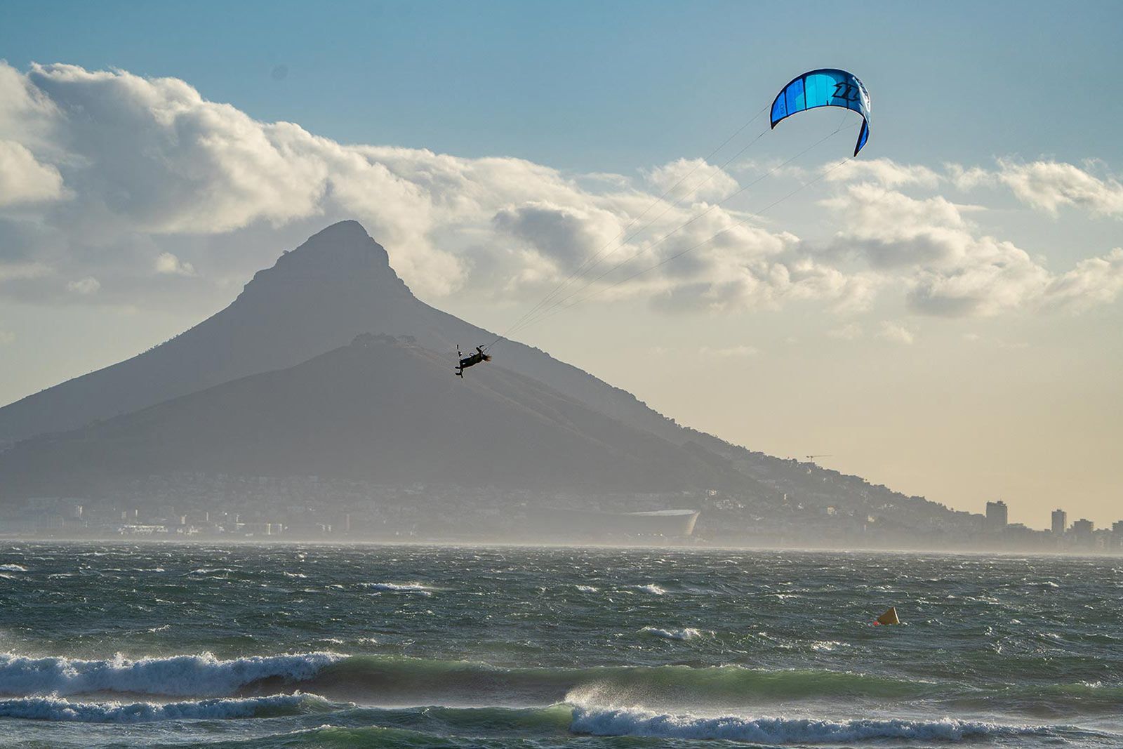 A person is flying a kite over the ocean with a mountain in the background.