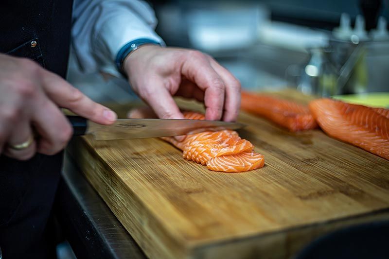 A person is cutting salmon on a wooden cutting board.