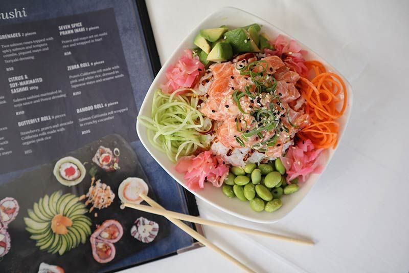 A bowl of sushi with chopsticks next to a menu.