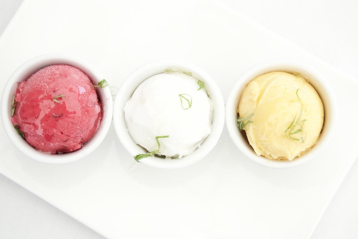 Three bowls of different flavors of ice cream are lined up on a white plate.