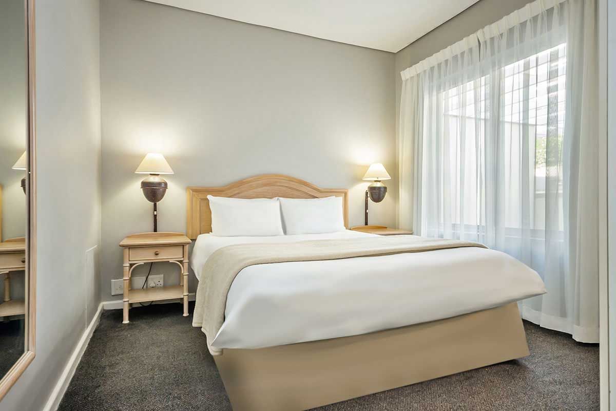 Ein Hotelzimmer mit Bett, Nachttisch, Spiegel und Fenster.