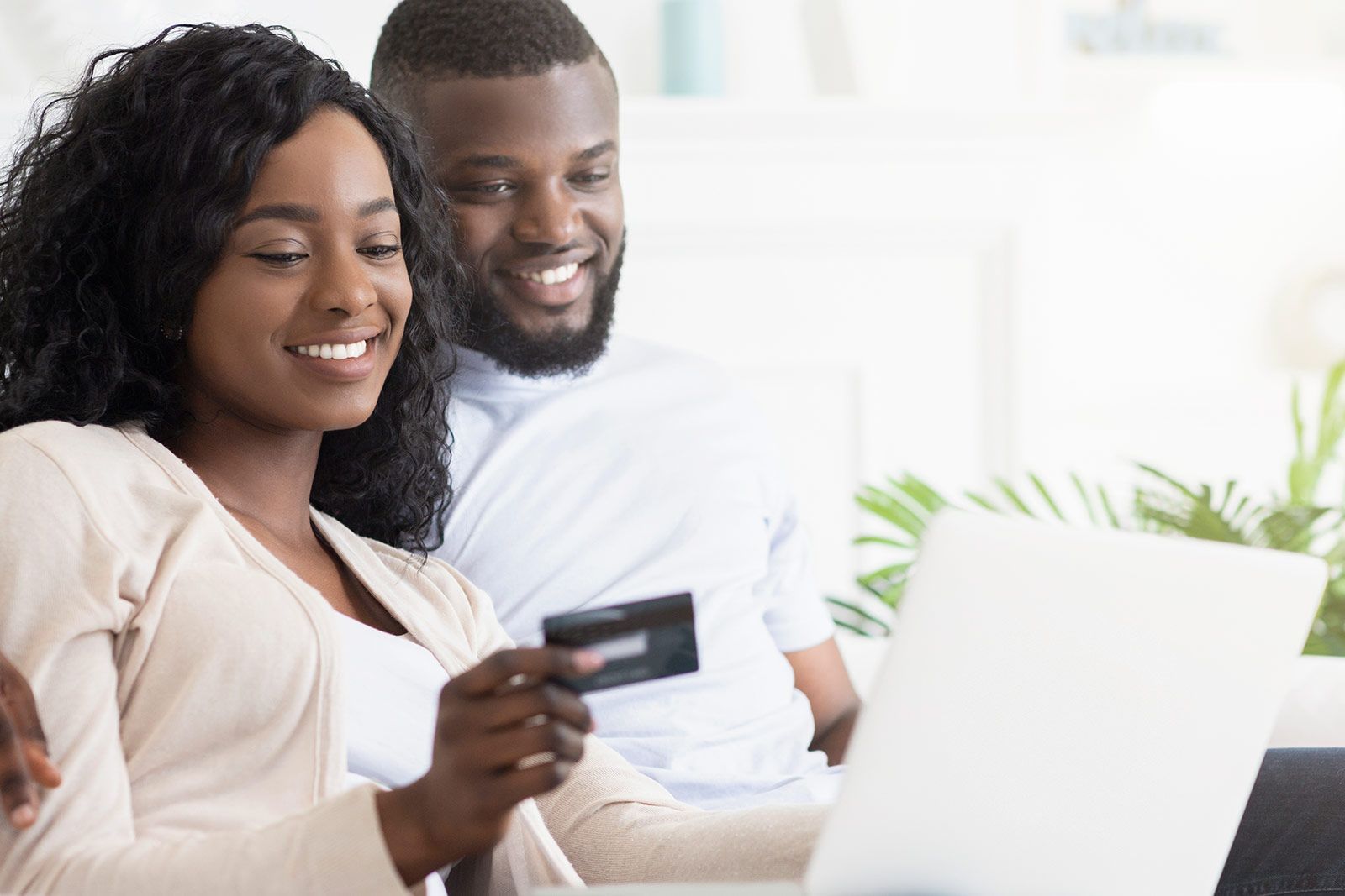 Un uomo e una donna sono seduti su un divano e usano un computer portatile e una carta di credito.