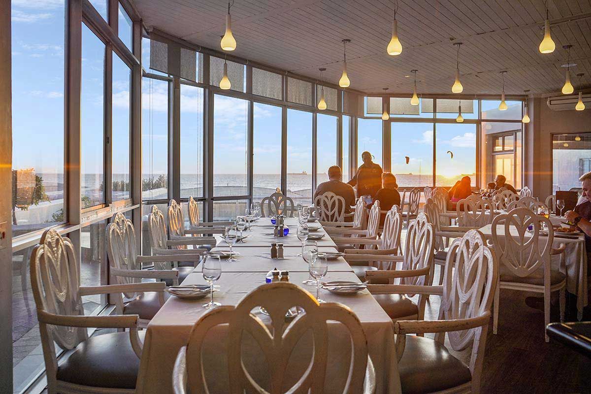 Ein Restaurant mit einem langen Tisch und Stühlen und Blick auf den Ozean.