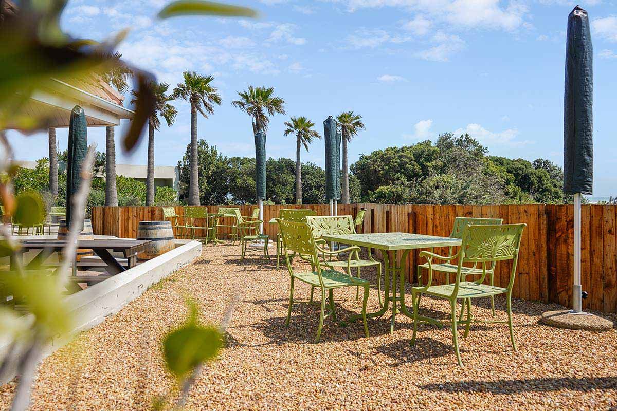 Eine Terrasse mit Tischen und Stühlen und Palmen im Hintergrund.