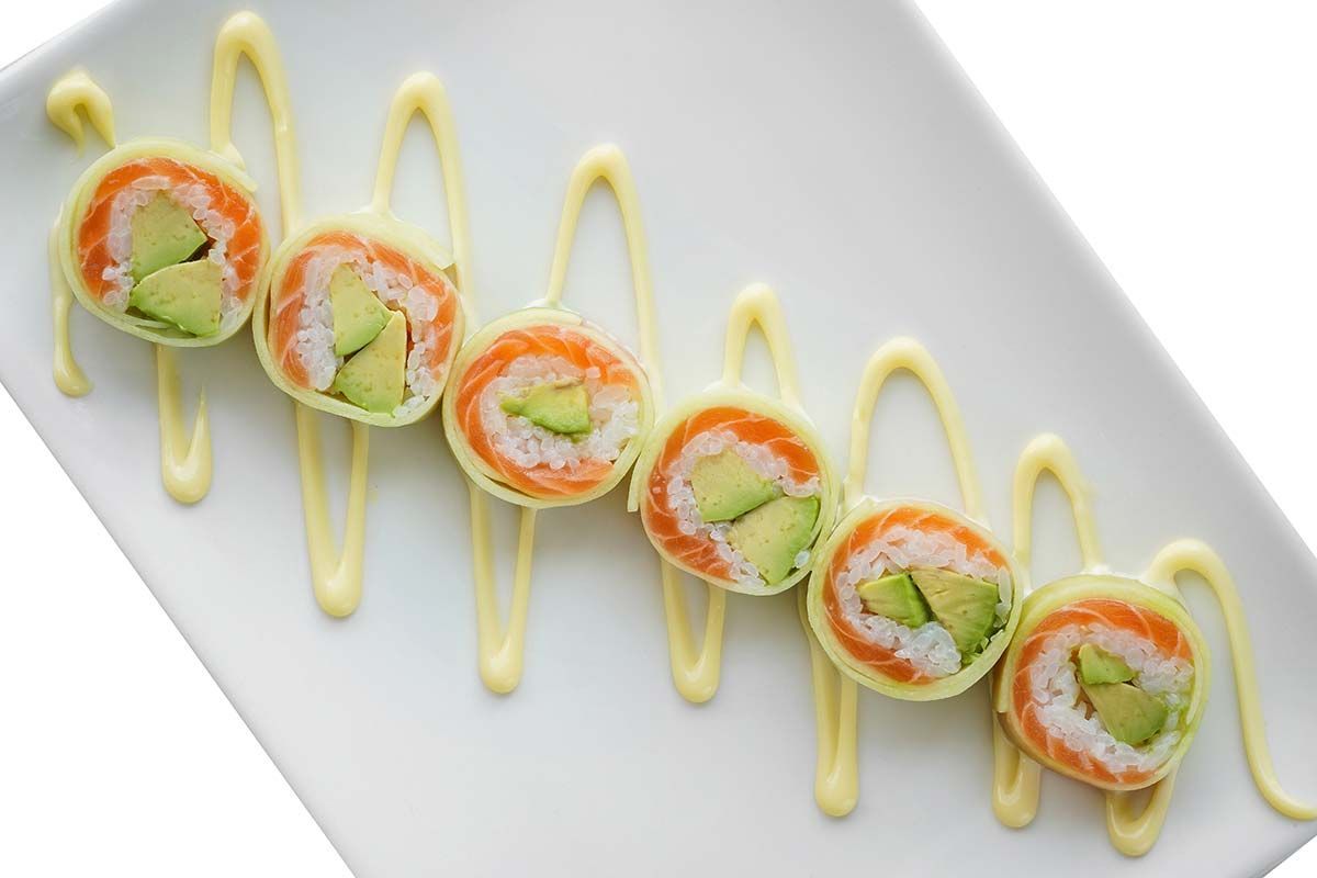 Eine Reihe Sushi-Rollen mit Avocado, Lachs und Mayonnaise auf einem weißen Teller.