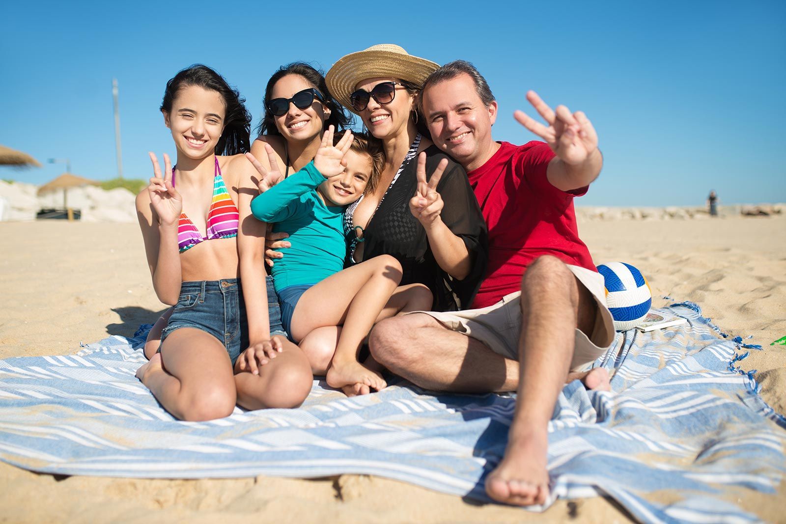 Una famiglia è seduta su una coperta sulla spiaggia e fa segni di pace.