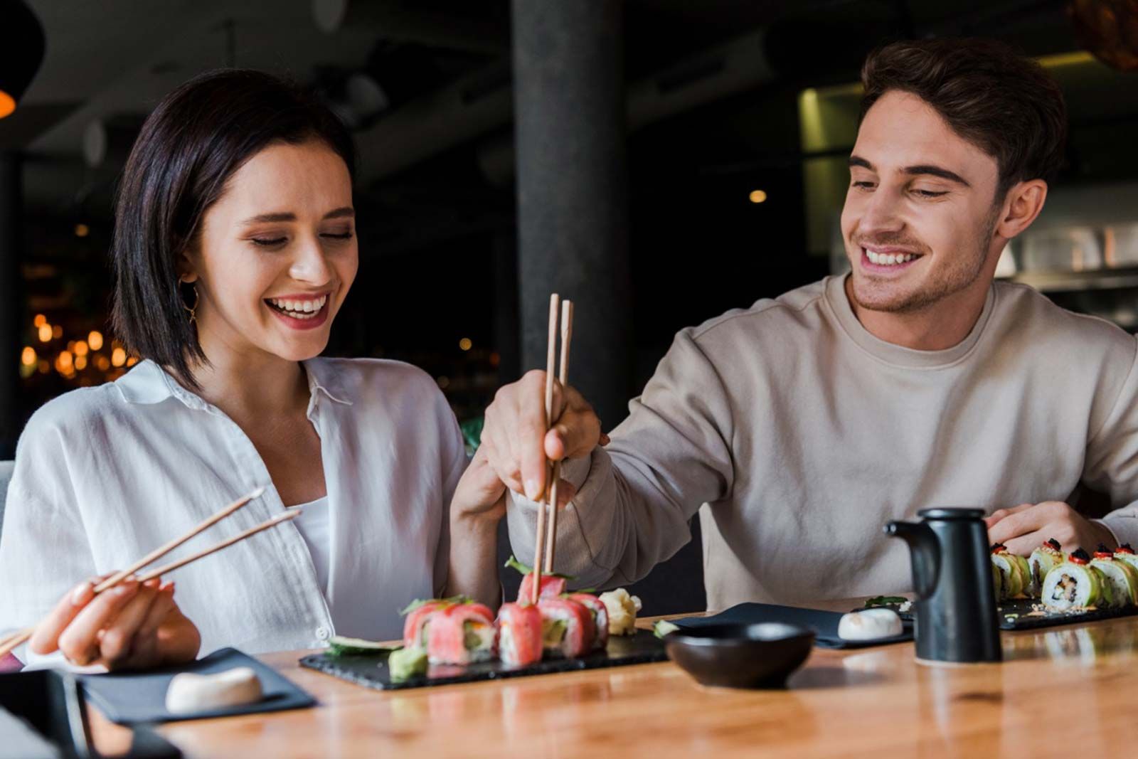 A man and a woman are sitting at a table eating sushi with chopsticks.