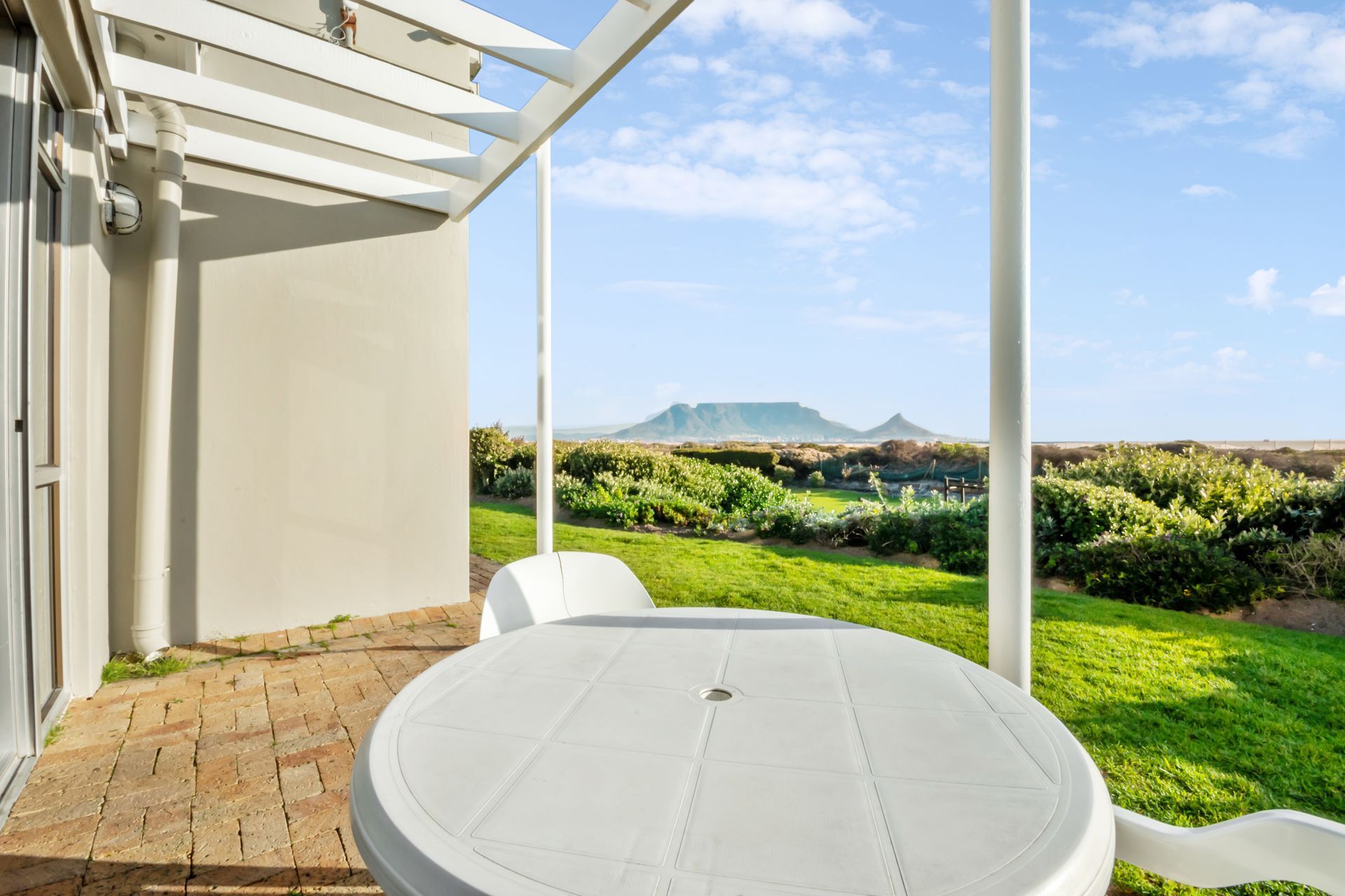 A white table and chairs on a patio with a view of a lush green field.