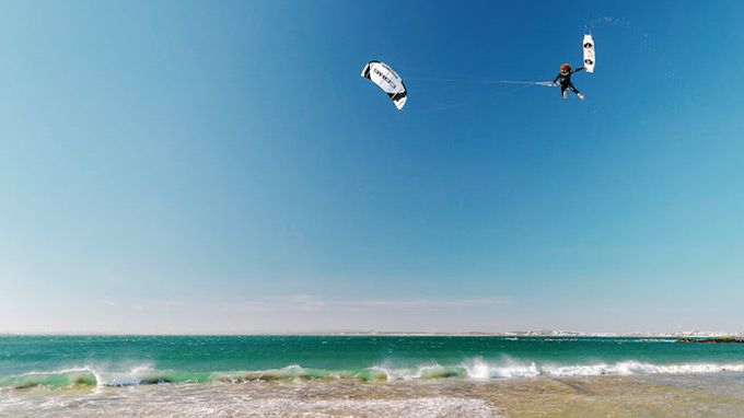 A couple of people are flying kites over the ocean.