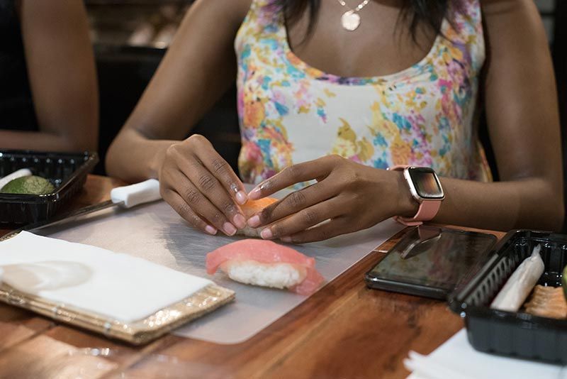 A woman is sitting at a table making sushi.