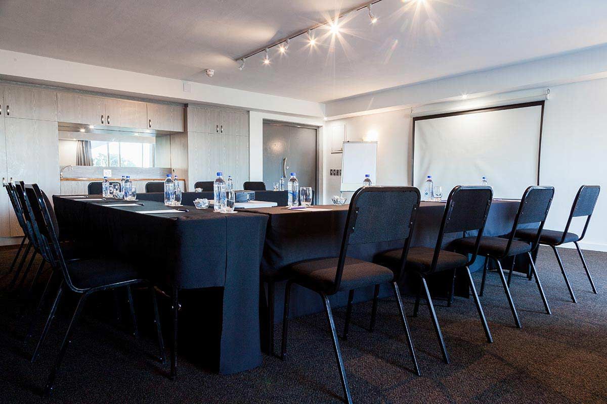 Ein Konferenzraum mit einem langen Tisch und Stühlen sowie einer Projektionsleinwand.