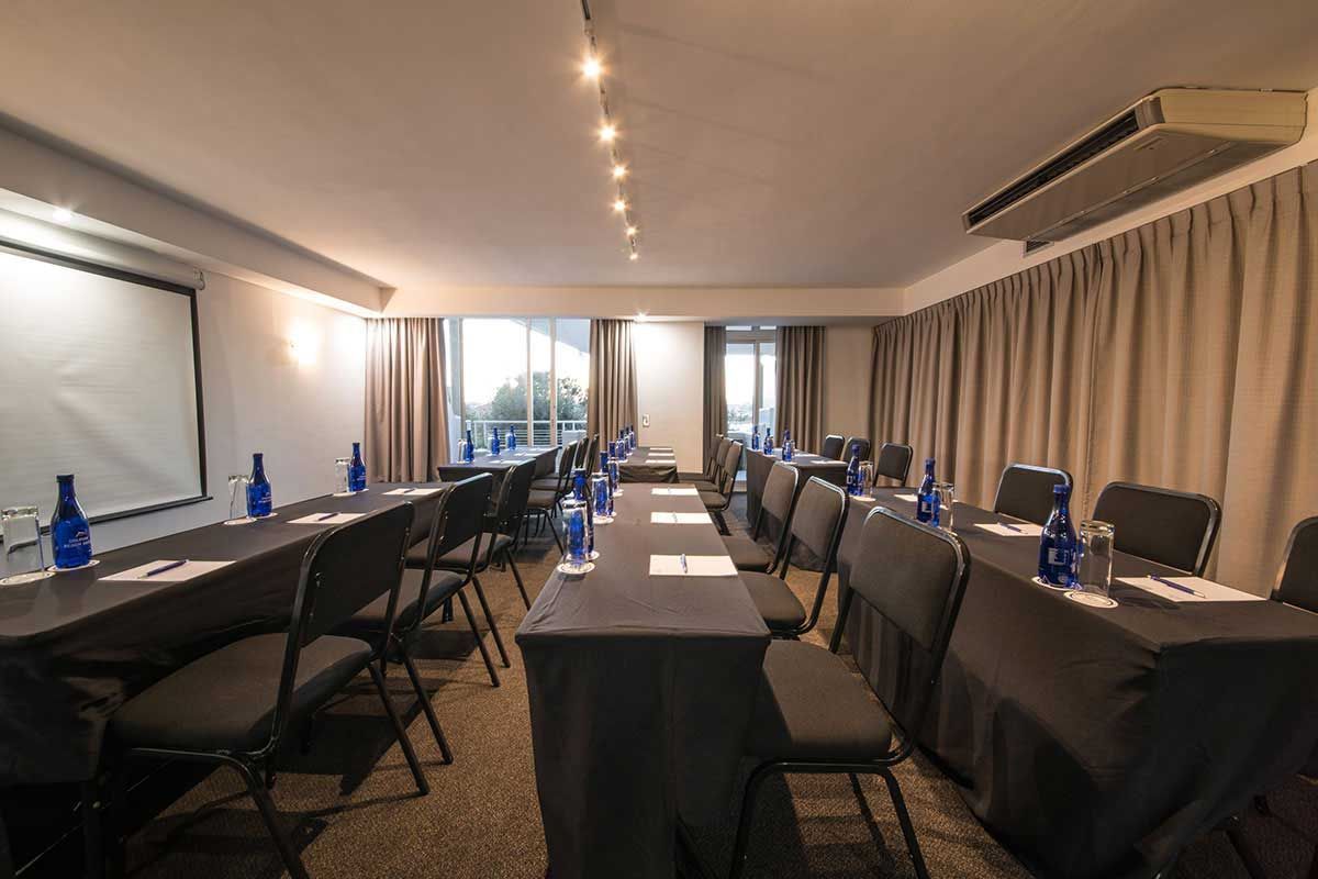 Ein Konferenzraum mit langen Tischen und Stühlen sowie einer Projektionsleinwand.