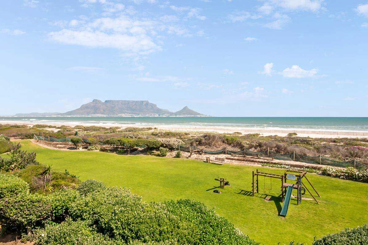 Ein Blick auf einen Strand mit einem Spielplatz im Vordergrund und einem Berg im Hintergrund.