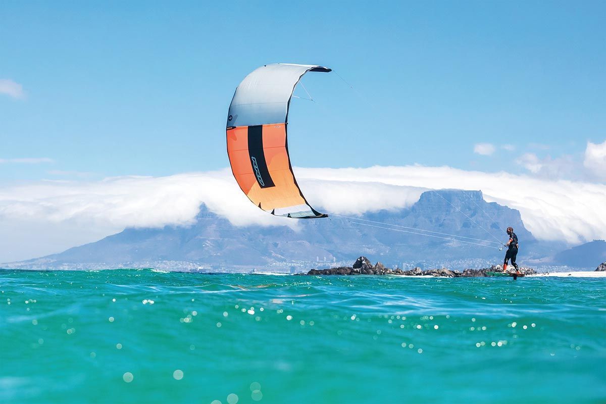 Eine Person lässt im Meer einen Drachen steigen . Im Hintergrund ist ein Berg zu sehen.