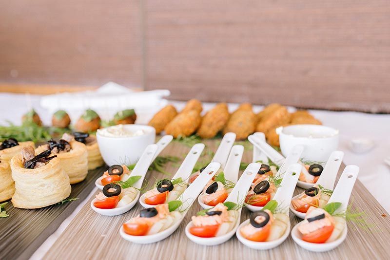 A buffet table with a variety of food on spoons.