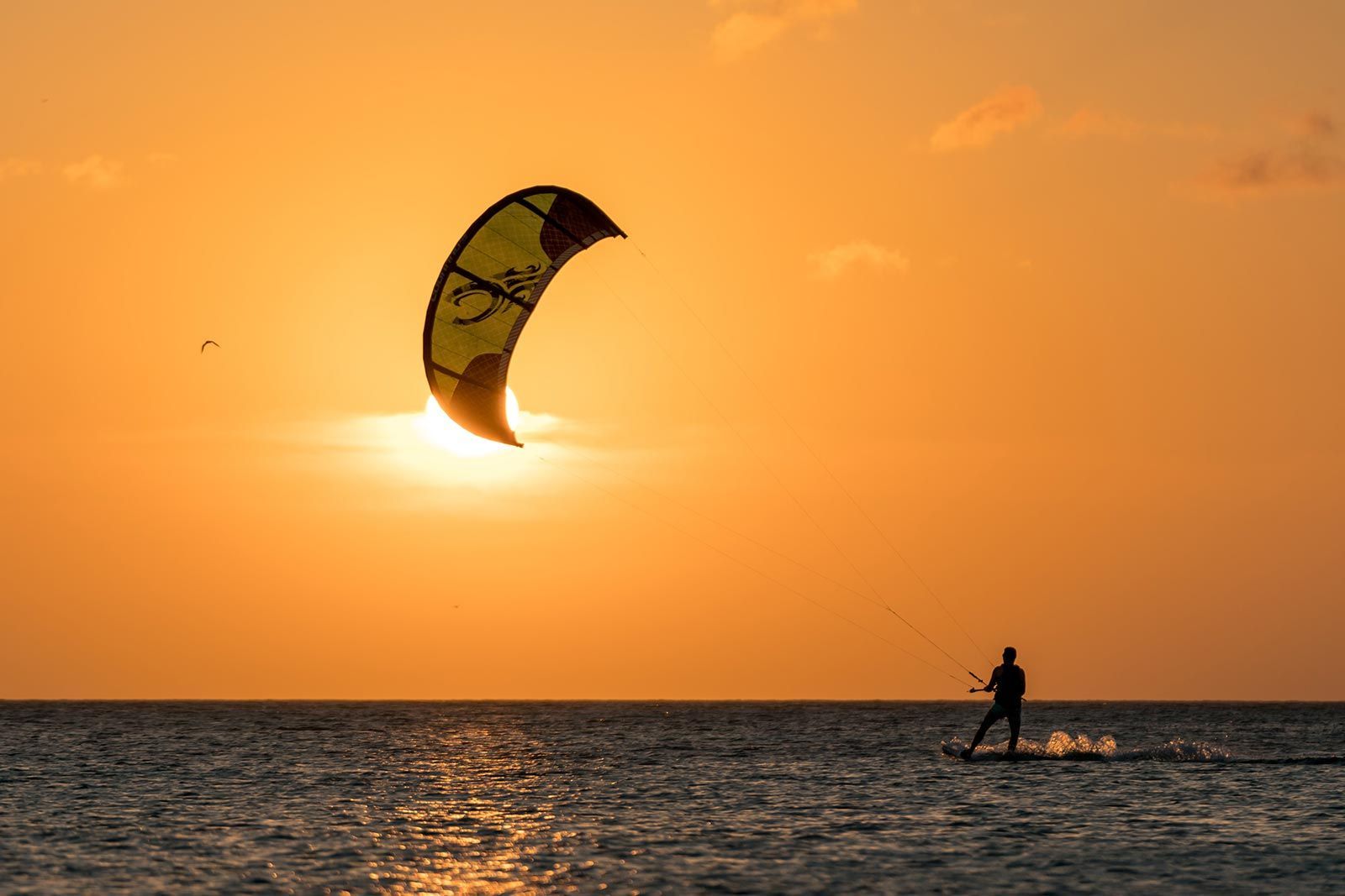 Een man laat een vlieger op in de oceaan bij zonsondergang.