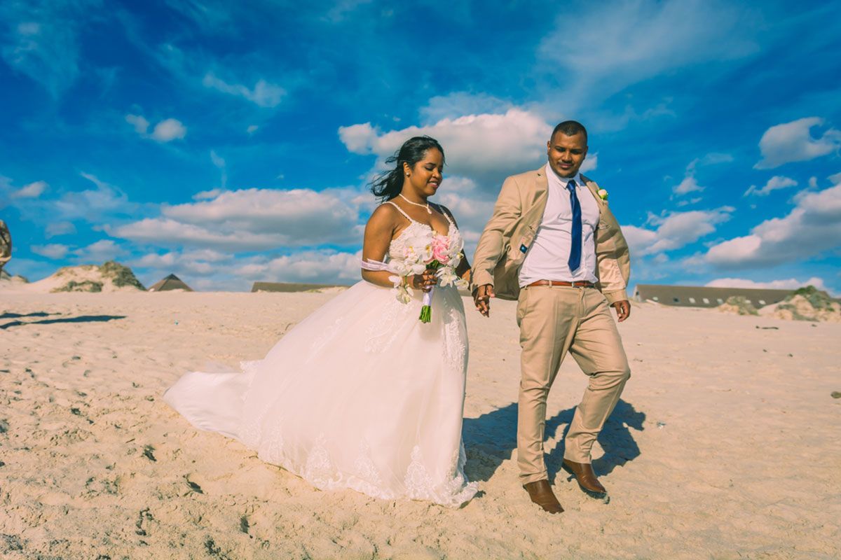 A bride and groom are walking on the beach.