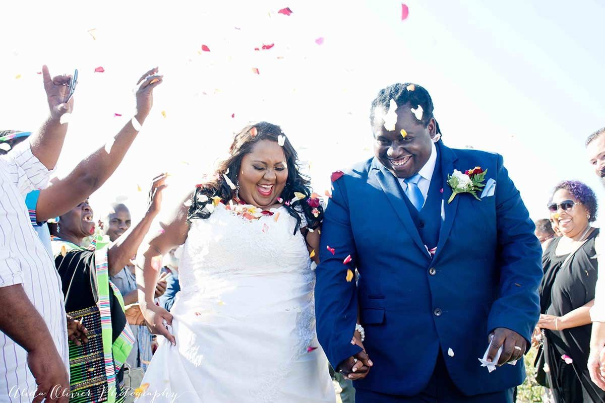A bride and groom are walking down the aisle surrounded by confetti.