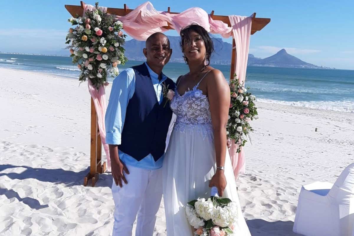 A bride and groom are posing for a picture on the beach.