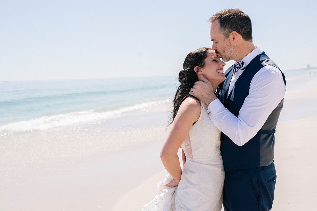 A bride and groom are kissing on the beach.