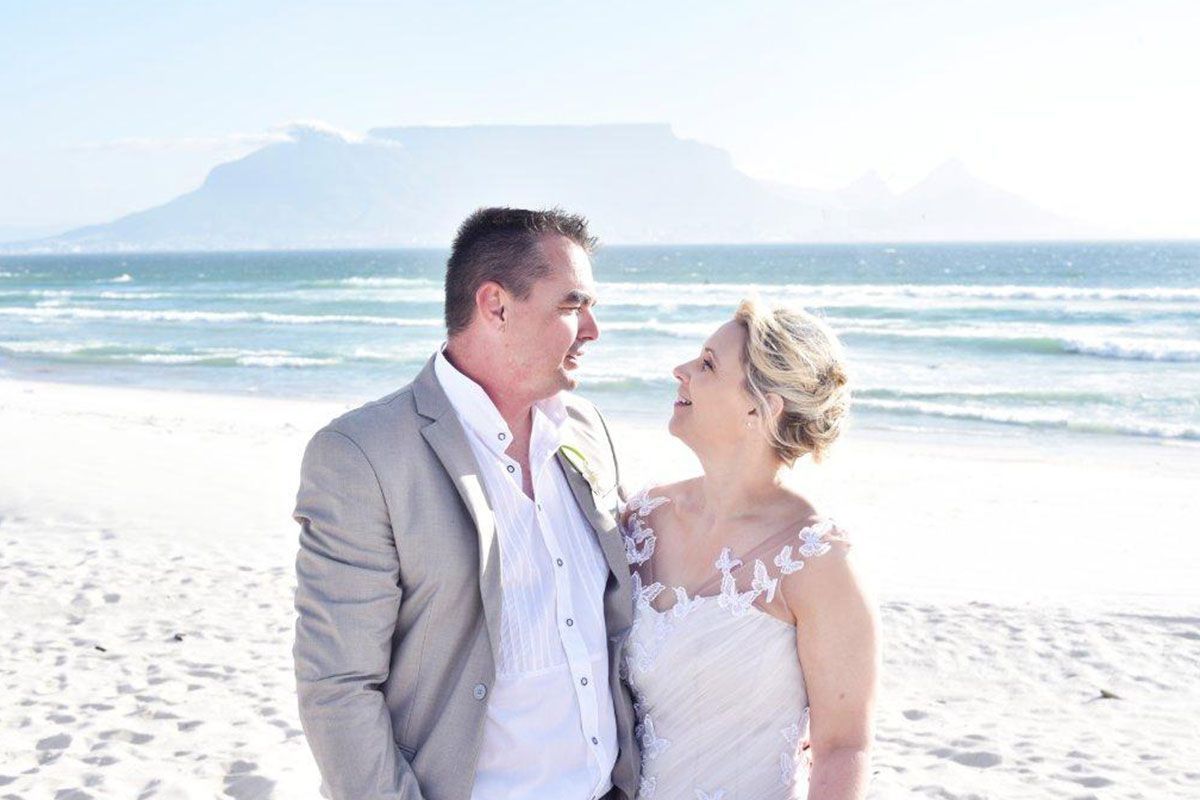 A bride and groom are standing on a beach looking at each other.