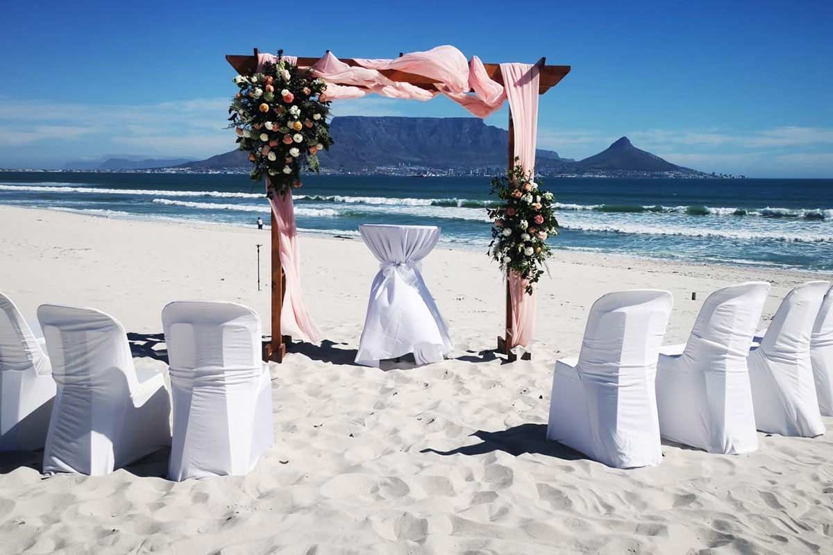 A wedding ceremony is taking place on the beach with a mountain in the background.