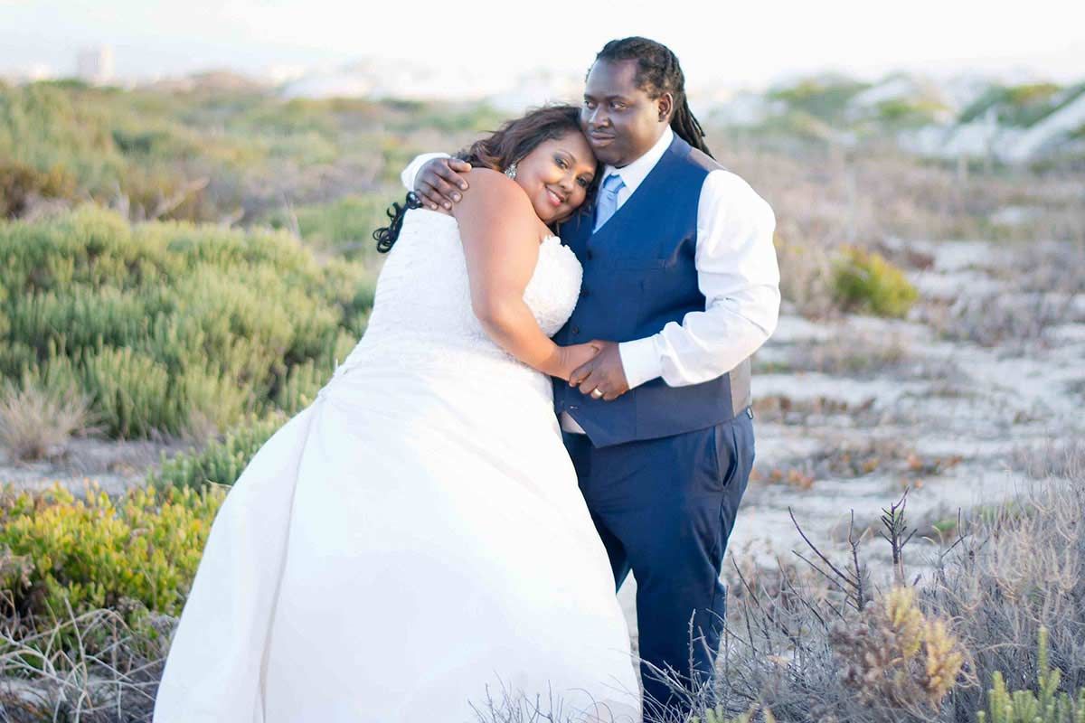 A bride and groom are hugging each other in a field.