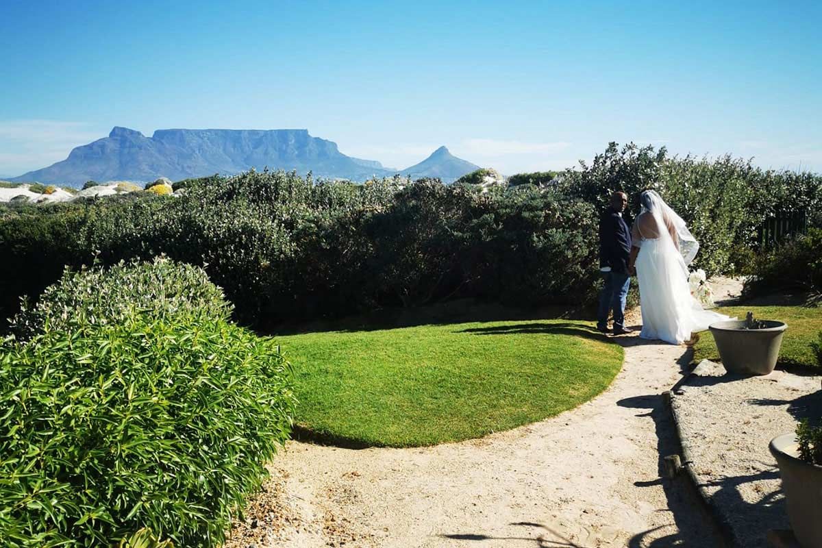 A bride and groom standing on a path with a mountain in the background