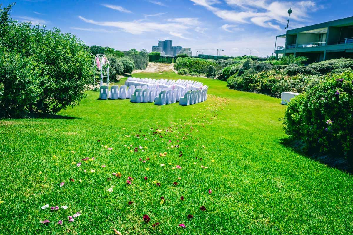 A row of white chairs are lined up in a lush green field.