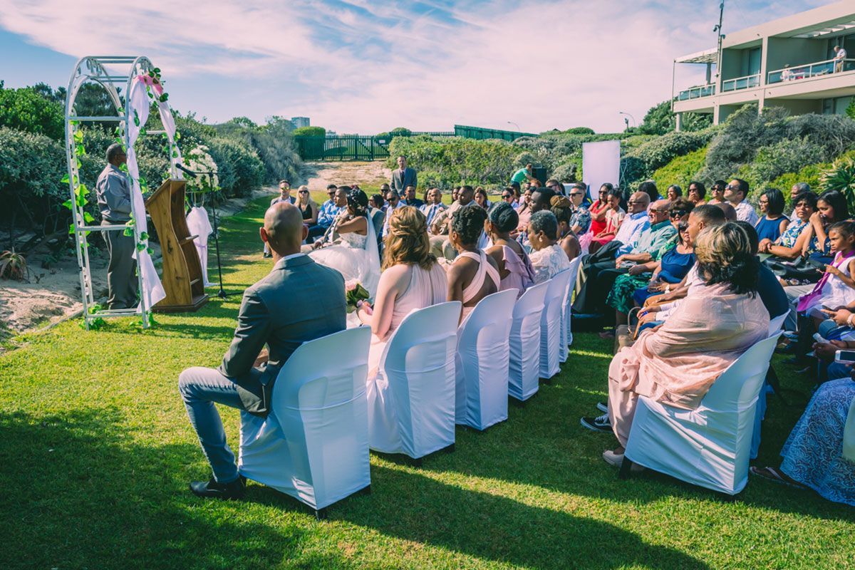 A group of people are sitting in white chairs at a wedding ceremony.