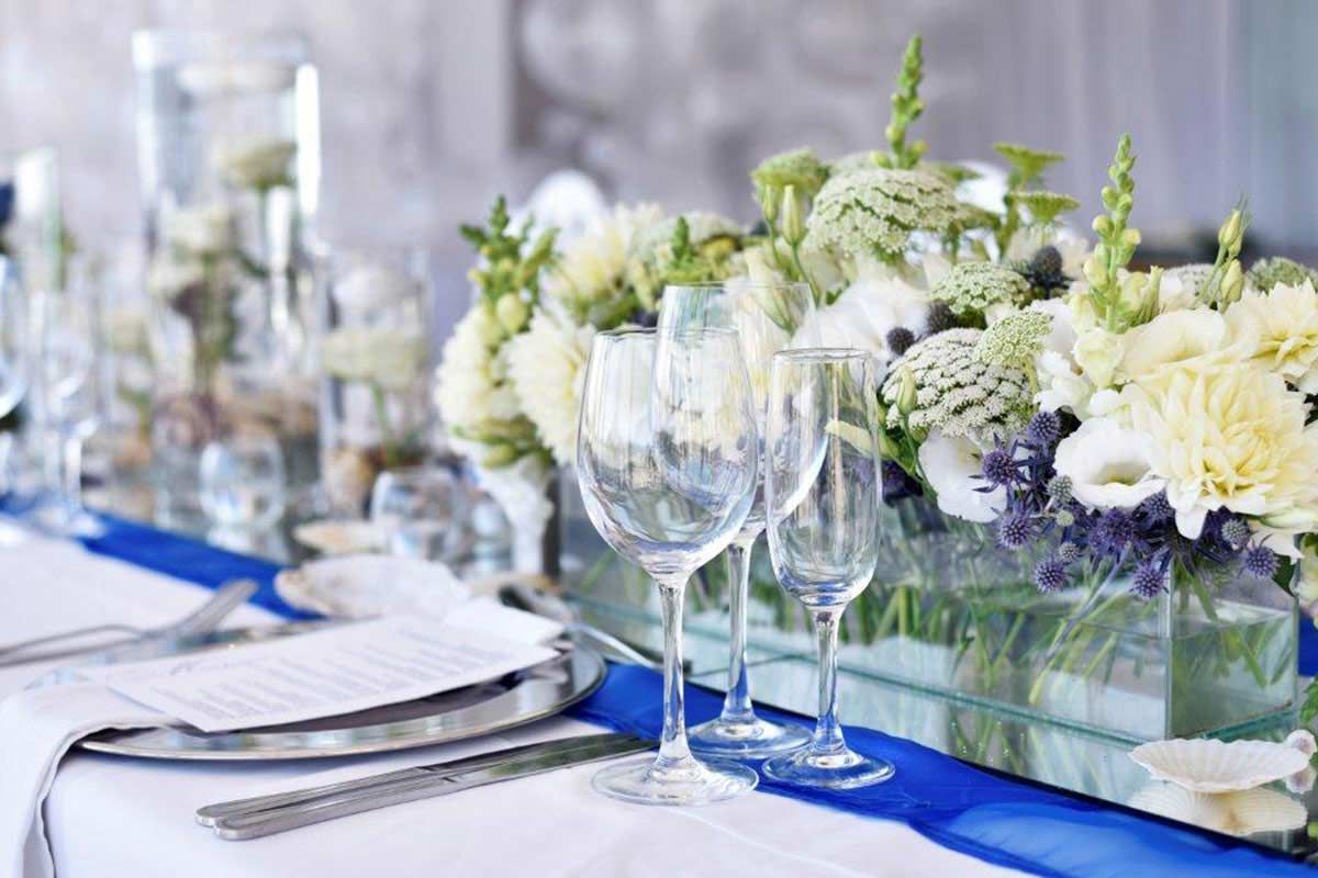 A long table with a vase of flowers and wine glasses on it.
