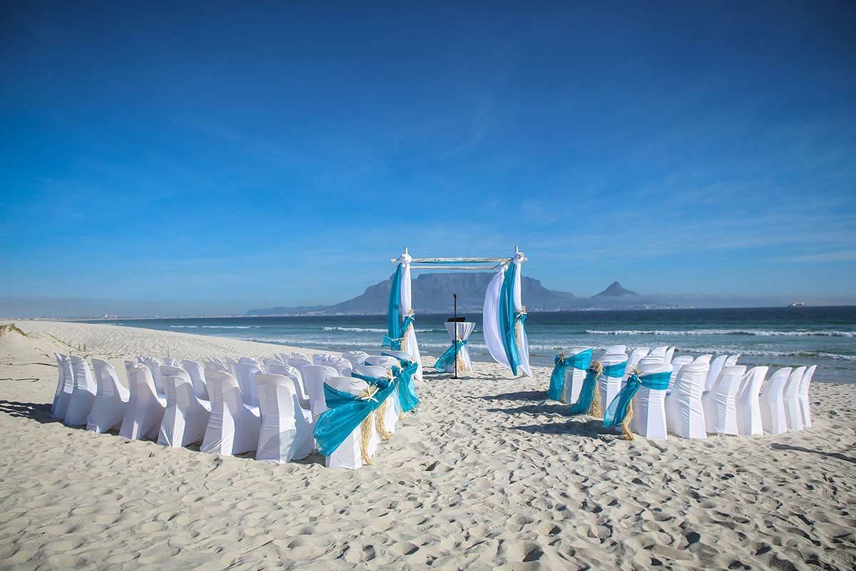 A row of white chairs are lined up on a beach.