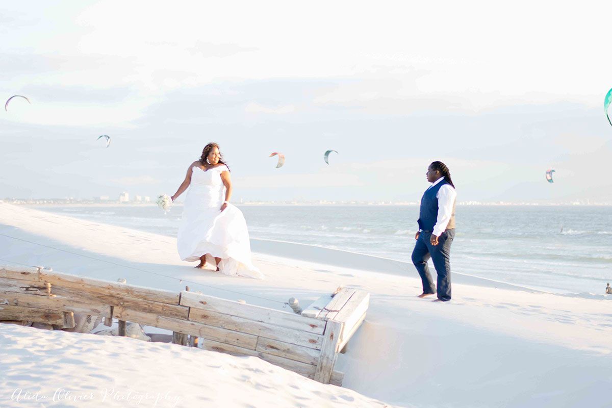 A bride and groom are standing on a dock on the beach.