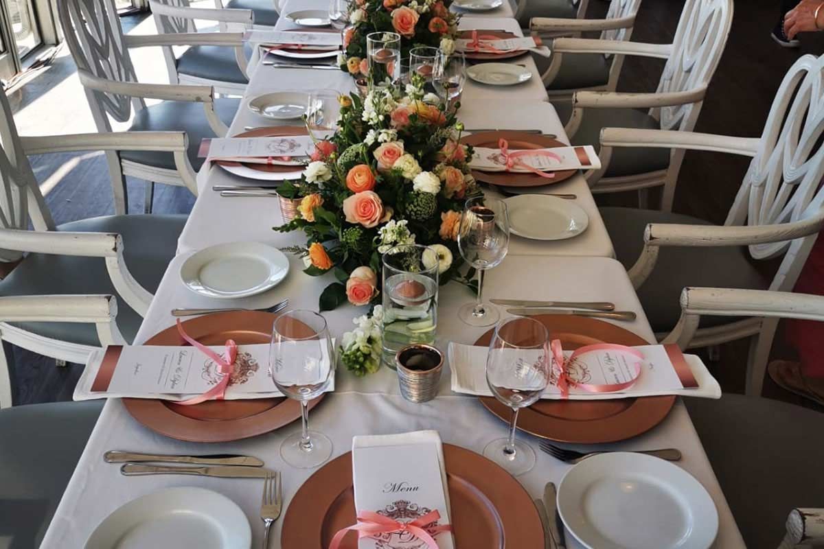 A long table with plates , utensils , and flowers on it.
